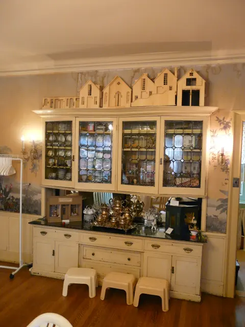 A glass display cabinet filled with miniature dolls and dollhouse furniture at a doll museum